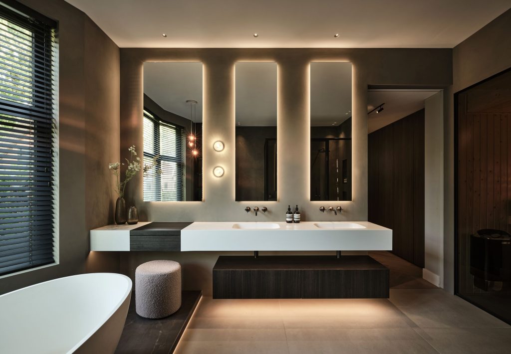 Luxe maatwerk badkamermeubel met dubbele HI-MACS wastafel, verlichte spiegels en Decolegno houtafwerking in een woonboerderij in Roden, ontworpen door DUIN Interior en gerealiseerd door A&F Interieurbouw.