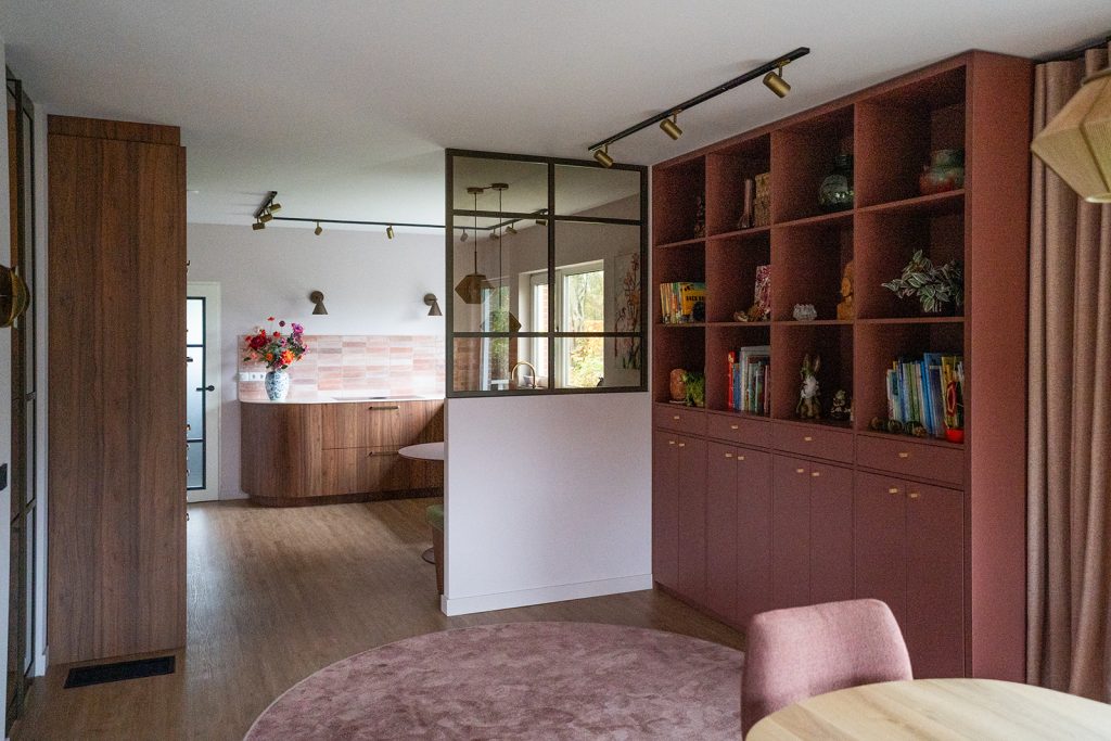 Maatwerk kastenwand in warme roze tint met geïntegreerde opbergruimte en stalen roomdivider in een woonhuis in Winschoten, ontworpen door Studio Vogt en gerealiseerd door A&F Interieurbouw. Groningen