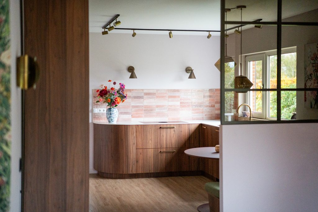Maatwerk keuken met warme houttinten, afgeronde vormen, roze wandtegels en geïntegreerde eethoek in een woonhuis in Winschoten, ontworpen door Studio Vogt en gerealiseerd door A&F Interieurbouw. Groningen