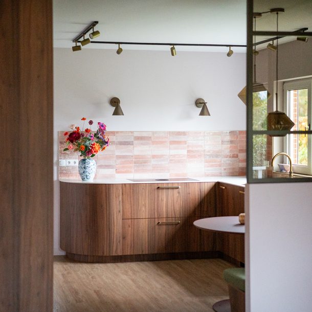 Maatwerk keuken met warme houttinten, afgeronde vormen, roze wandtegels en geïntegreerde eethoek in een woonhuis in Winschoten, ontworpen door Studio Vogt en gerealiseerd door A&F Interieurbouw. Groningen