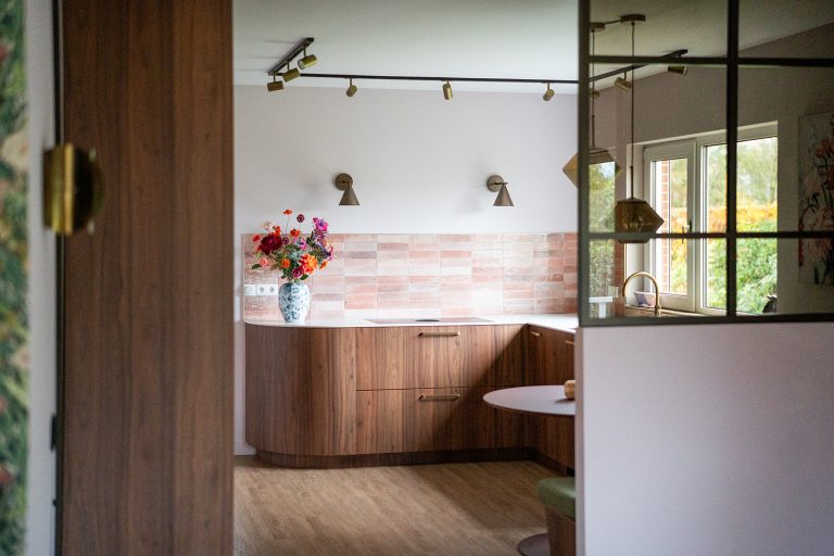 Maatwerk keuken met warme houttinten, afgeronde vormen, roze wandtegels en geïntegreerde eethoek in een woonhuis in Winschoten, ontworpen door Studio Vogt en gerealiseerd door A&F Interieurbouw. Groningen