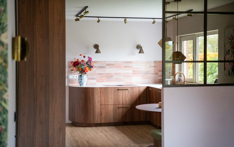 Maatwerk keuken met warme houttinten, afgeronde vormen, roze wandtegels en geïntegreerde eethoek in een woonhuis in Winschoten, ontworpen door Studio Vogt en gerealiseerd door A&F Interieurbouw. Groningen