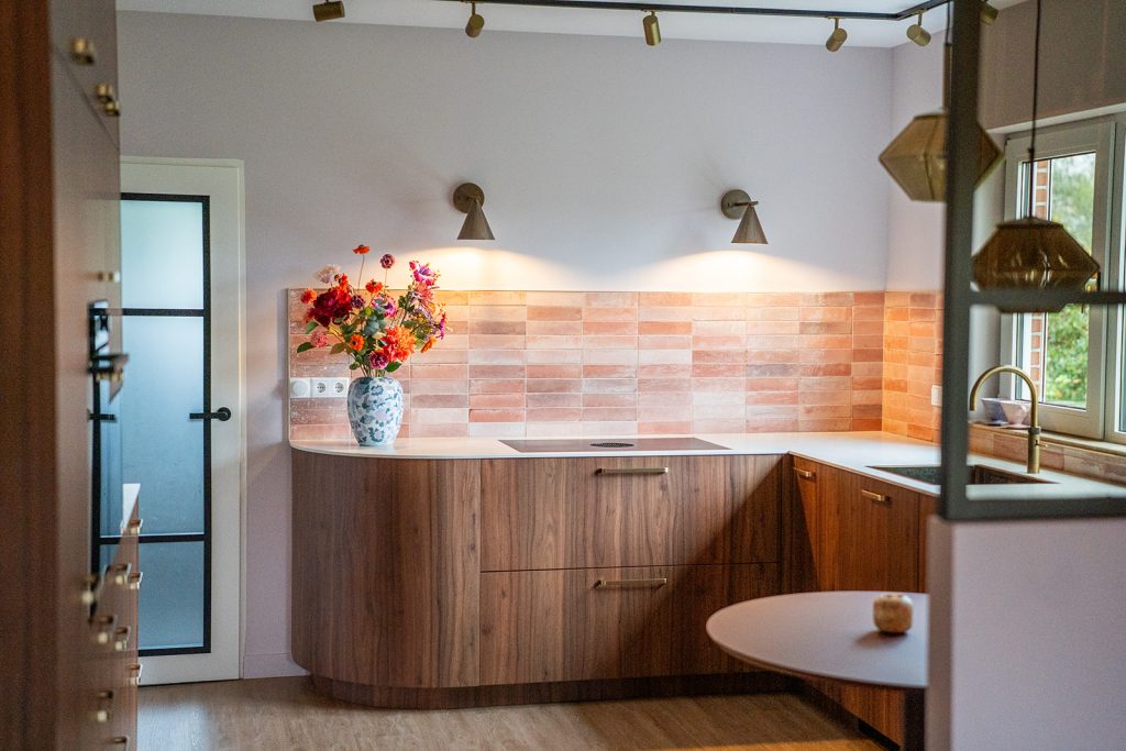 Maatwerk keuken met afgeronde fronten, warme houttinten, roze tegelwand en geïntegreerde eethoek in een woonhuis in Winschoten, ontworpen door Studio Vogt en gerealiseerd door A&F Interieurbouw. Groningen