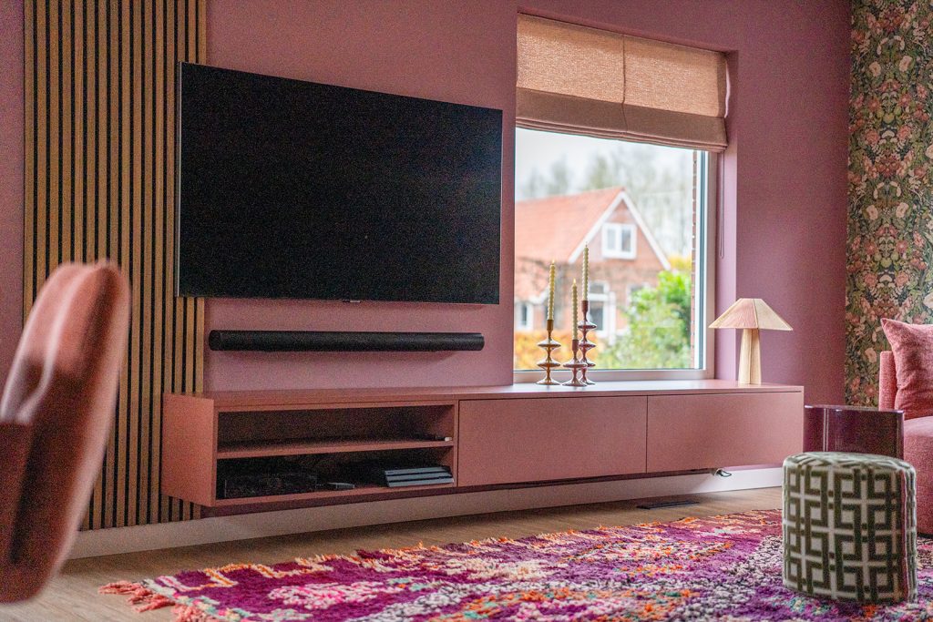 Maatwerk tv-meubel met zwevende opstelling, houten wandafwerking en warme roze accenten in een woonhuis in Winschoten, ontworpen door Studio Vogt en gerealiseerd door A&F Interieurbouw. Groningen