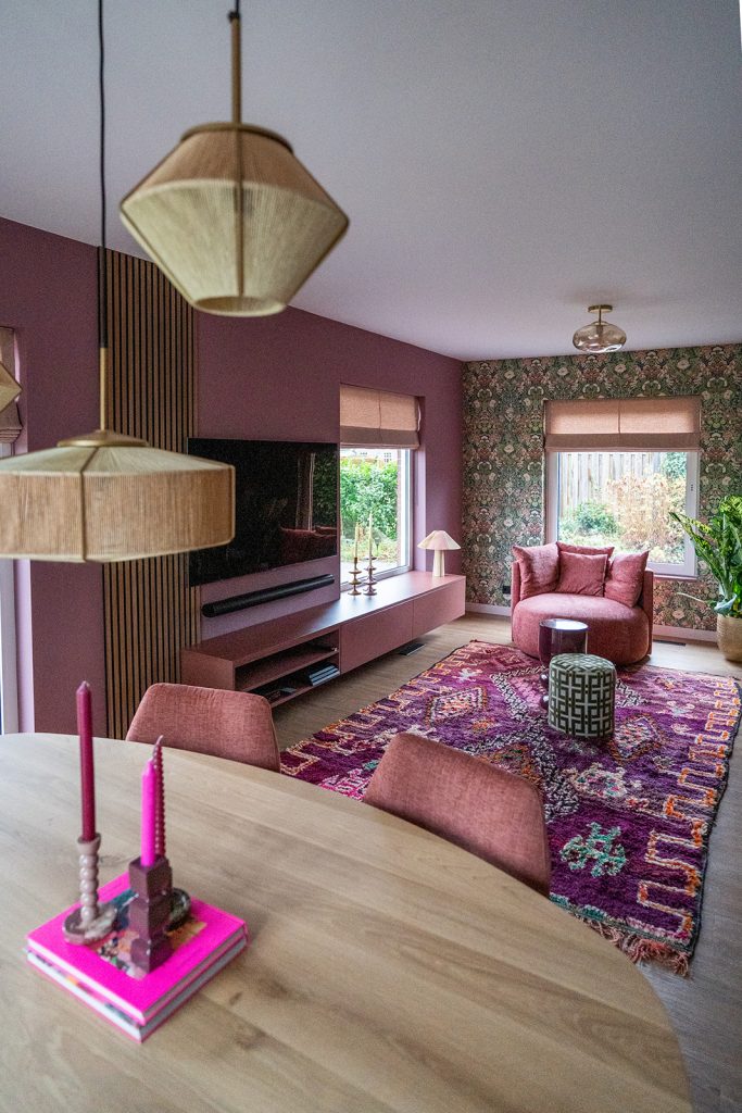 Maatwerk tv-meubel met houten lattenwand, warme roze tinten en geïntegreerde opbergruimte in een woonhuis in Winschoten, ontworpen door Studio Vogt en gerealiseerd door A&F Interieurbouw.